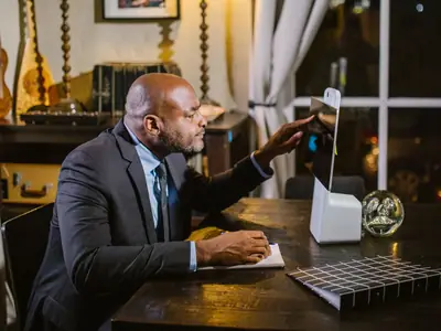 A Black man in a suit works at a computer in his home office in the evening.