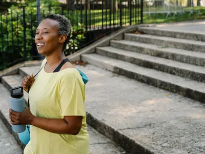 An older woman in a yellow T-shirt holds a blue water bottle outdoors.