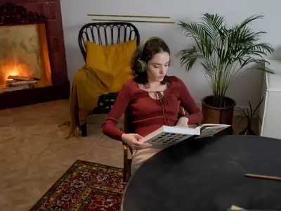 A woman in a red sweater reads a book while wearing headphones in a cozy living room.