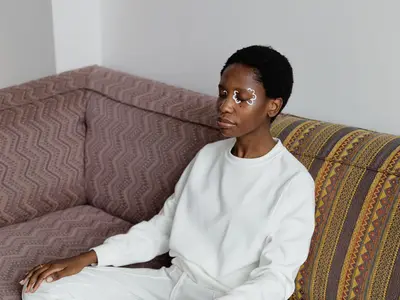 A woman sits cross-legged on a couch, meditating with her eyes closed.